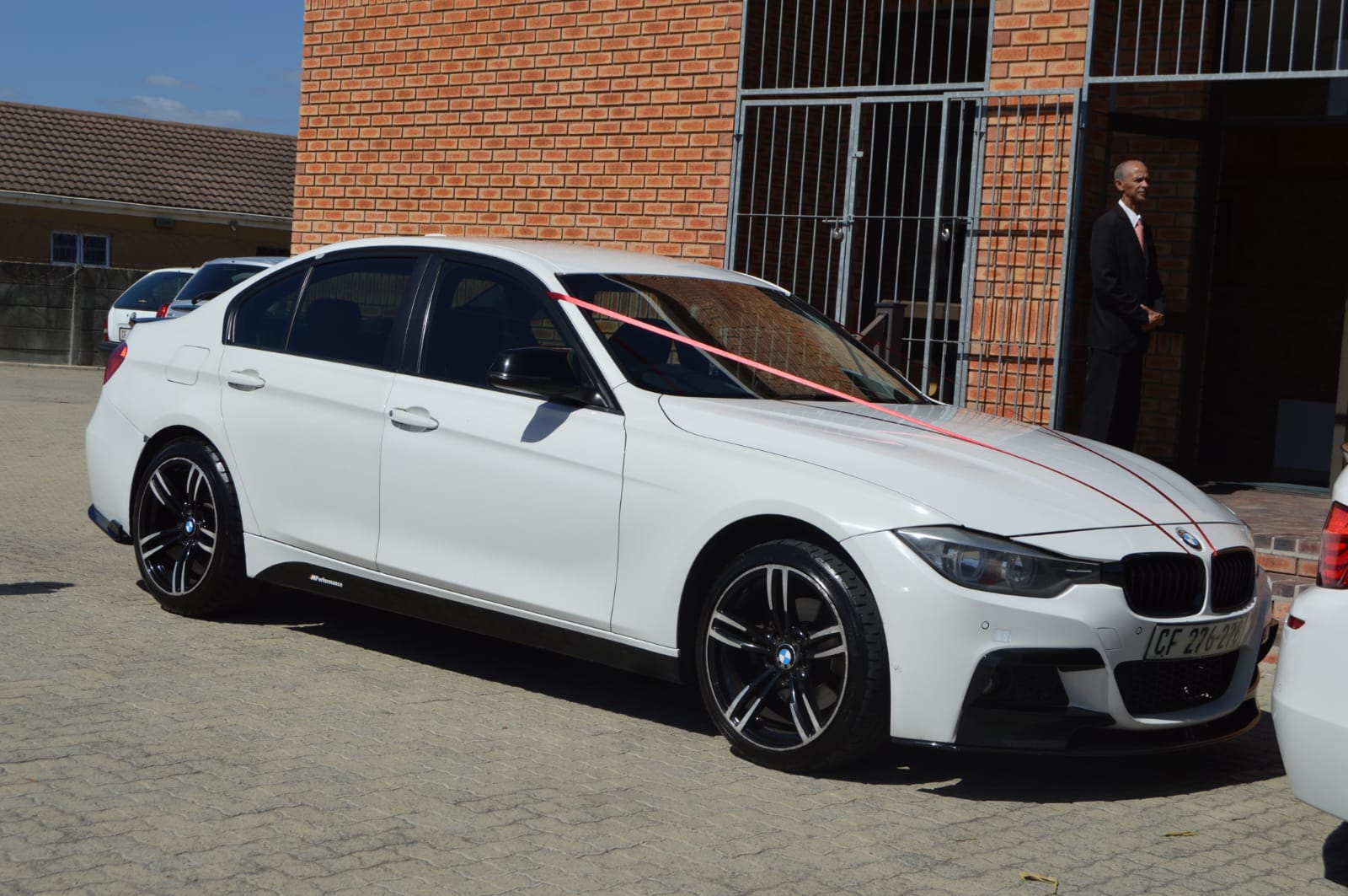 White BMW 3 Series M Sport with a red ribbon outside a church