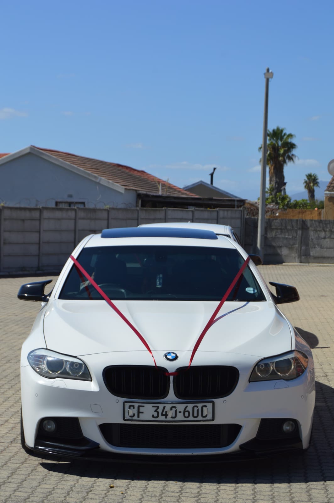 White BMW 5 Series photographed head on with red wedding ribbons