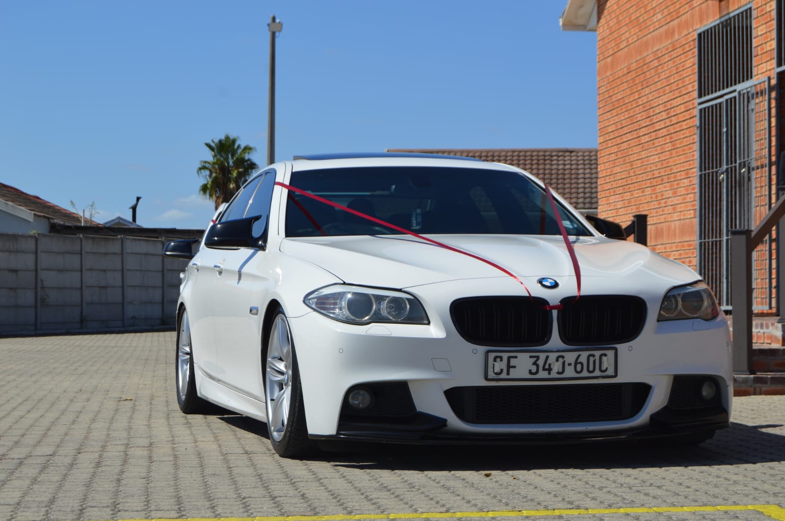 White BMW 5 Series M Sport dressed with a red wedding ribbon