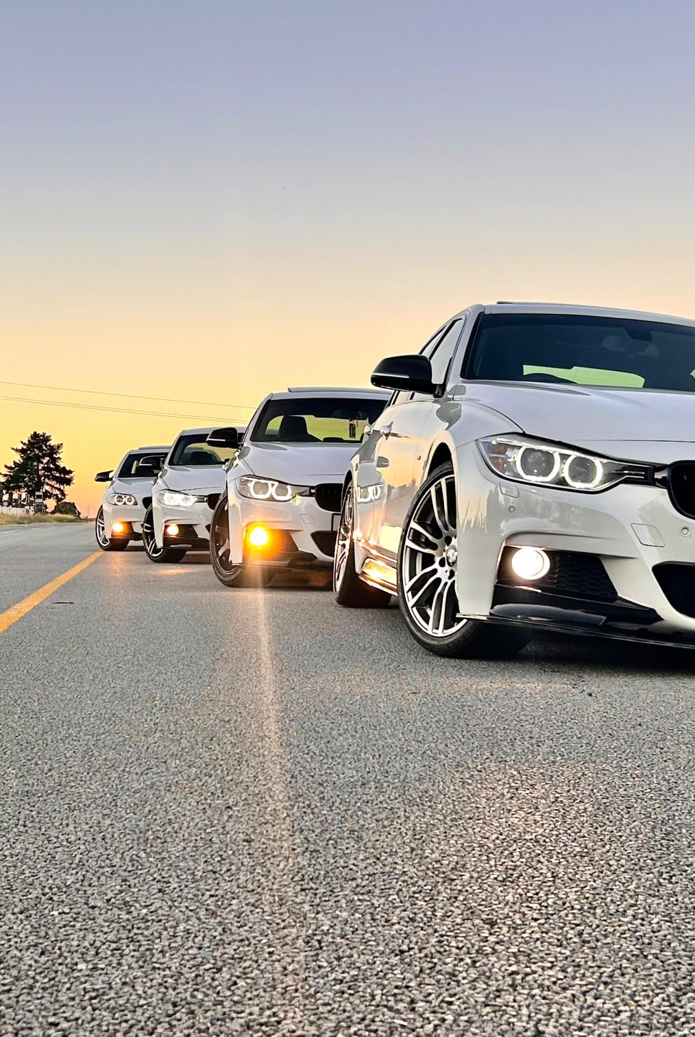 Four white BMWs travelling in convoy on an open road at sunset near Cape Town