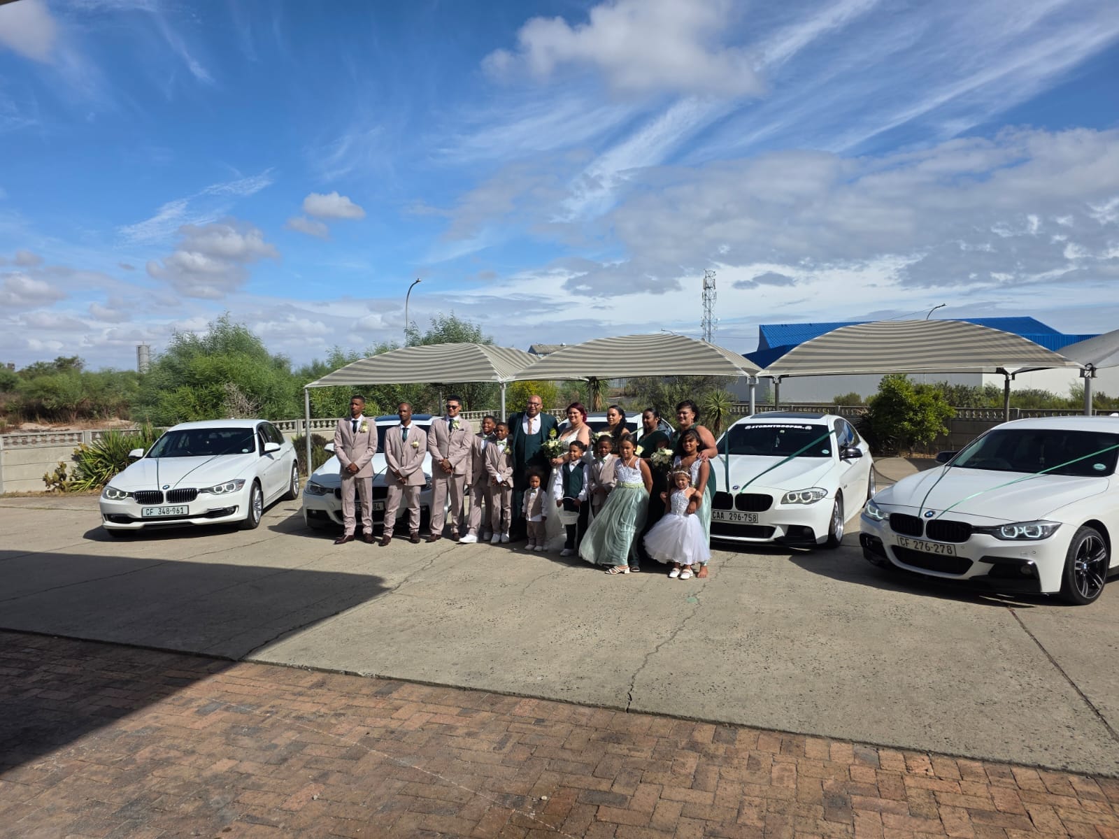 A full bridal party photographed in front of five white BMW cars